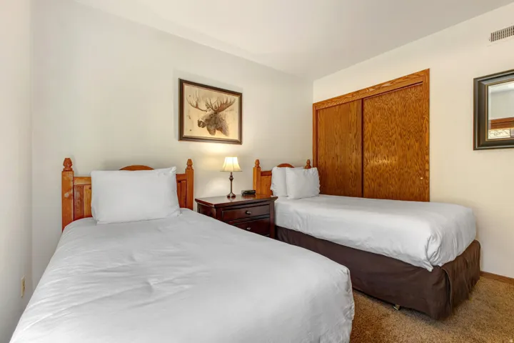 Bedroom featuring two twin beds with wood-finish headboards, a dark wood-finish nightstand, and a matching dark wood-finish closet with sliding doors