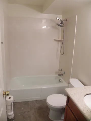 Bathtub with integrated shower surround, stainless steel showerhead, and tiled flooring