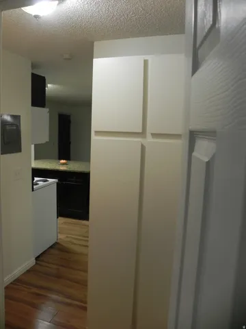 White cabinetry with a textured ceiling, wood-finish flooring, and white baseboards