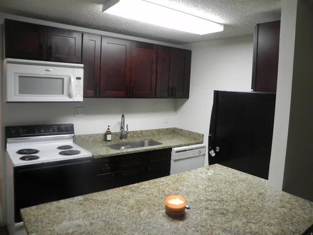 Kitchen featuring dark wood-finish cabinetry, light speckled countertops, a stainless steel sink with a gooseneck faucet, white built-in microwave, and black and white range