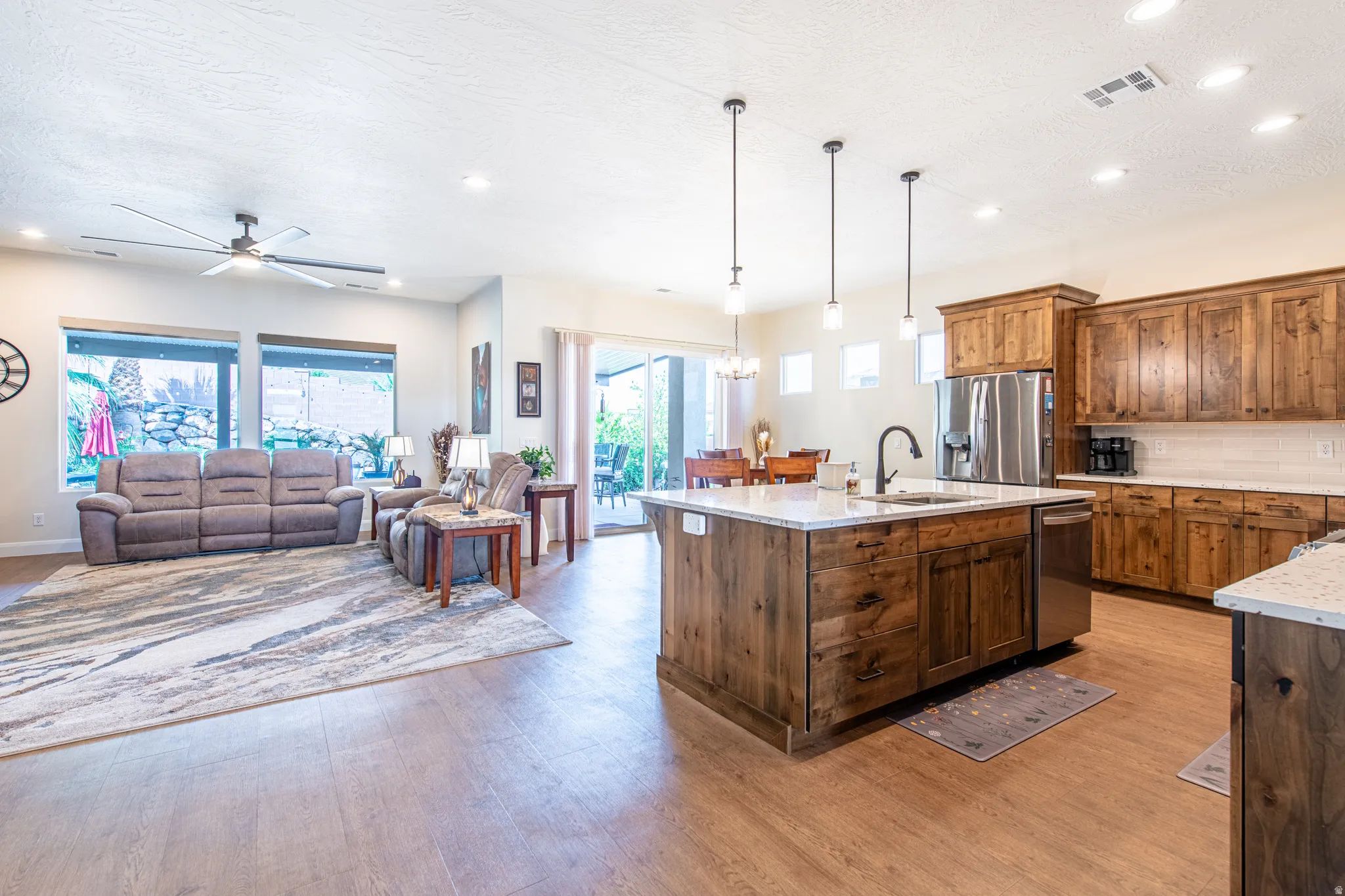 Open-concept living space featuring wood-finish flooring, a kitchen island with pendant lighting, stainless steel appliances, and wood cabinetry