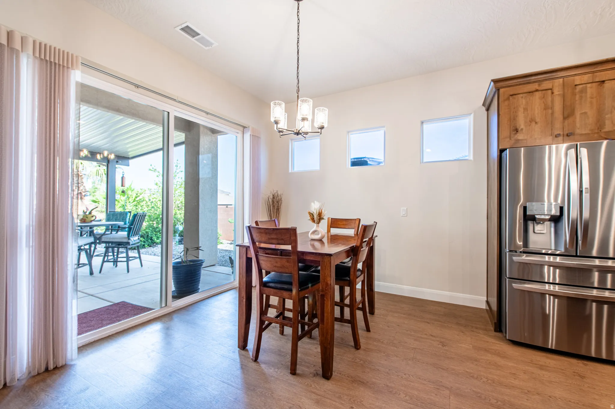 Wood-finish flooring, sliding glass patio doors, three transom windows, a chandelier light fixture, and wood cabinetry