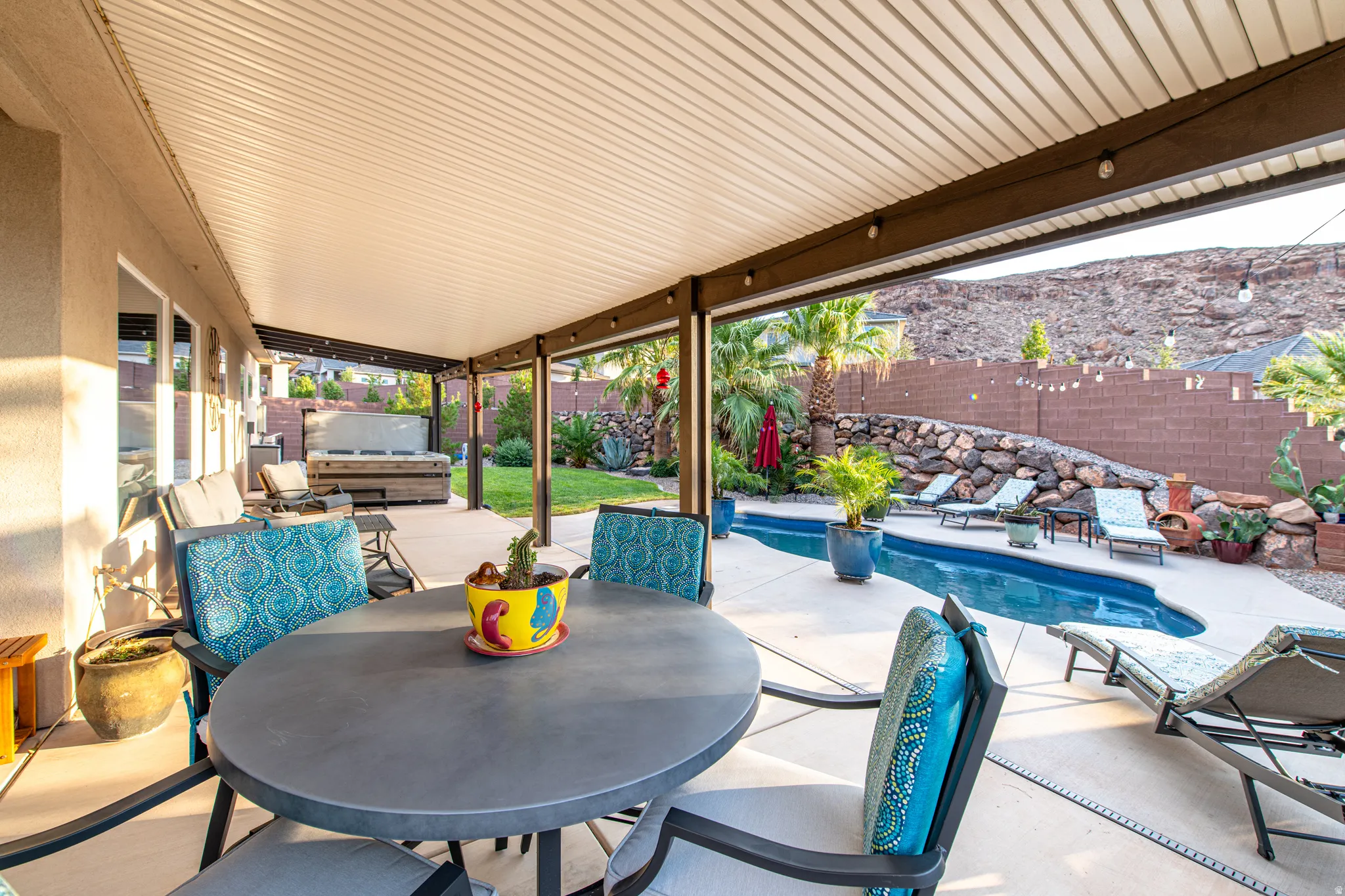 Covered patio with integrated lighting, outdoor spa, concrete patio, swimming pool, and stone retaining wall