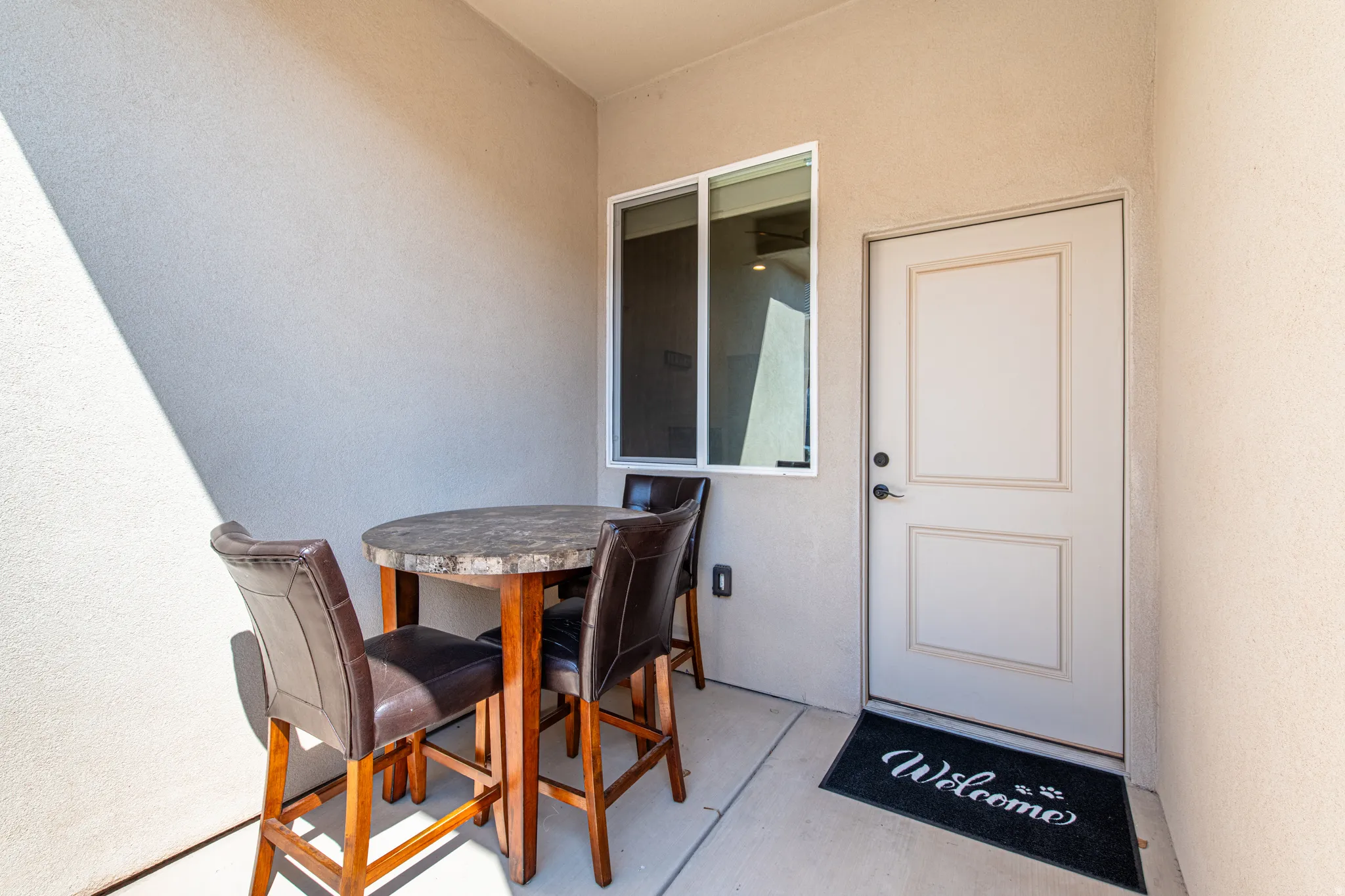 Outdoor patio space featuring stucco exterior, a white panel door, and a single-pane window