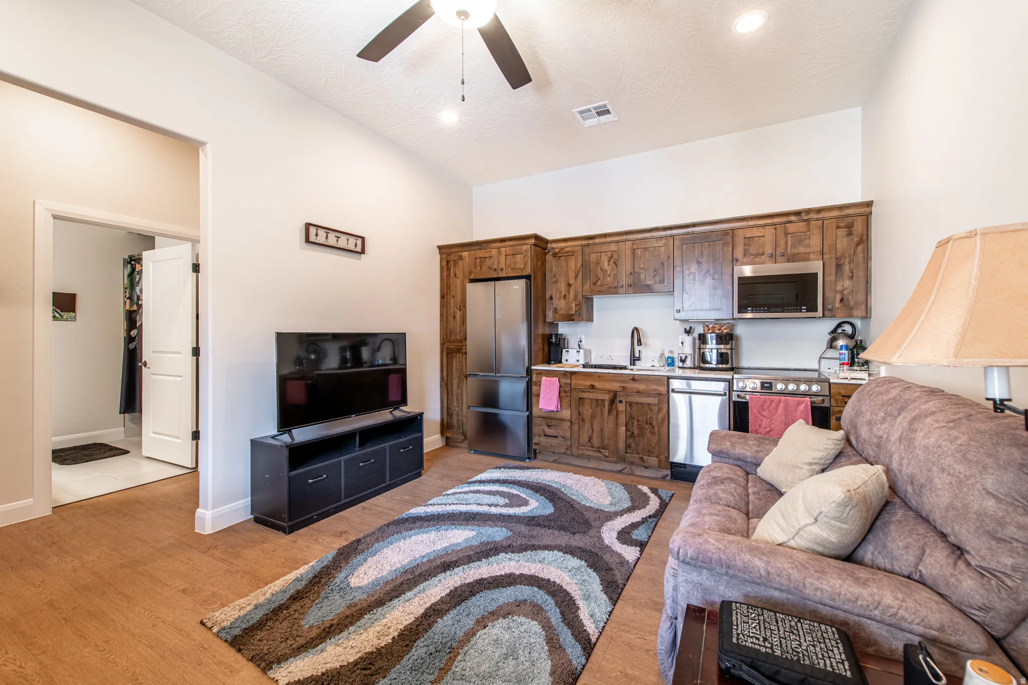 Integrated kitchen area with wood cabinetry, stainless steel appliances, and a ceiling fan