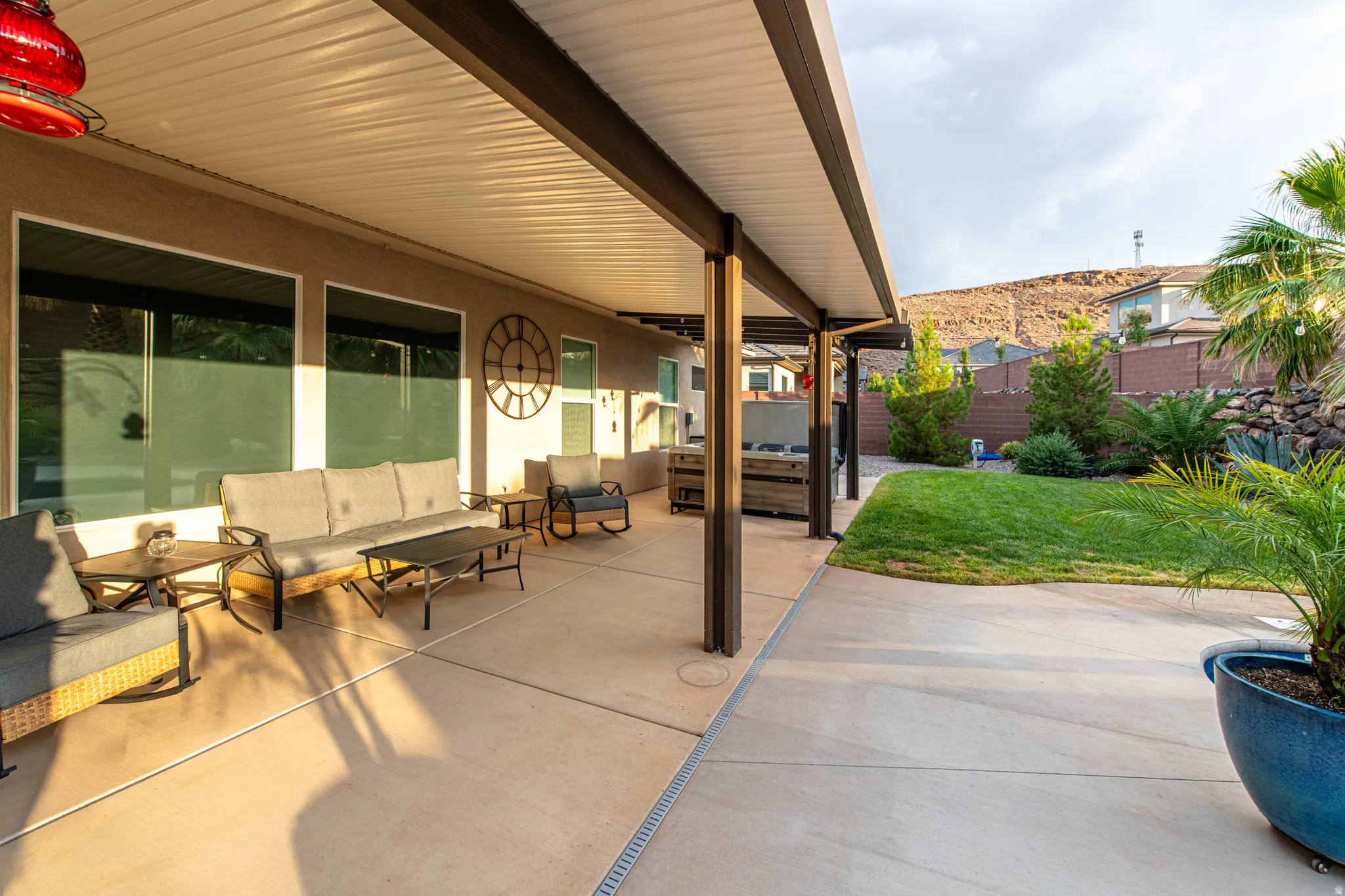 Expansive covered patio with concrete flooring, multiple large windows, and a landscaped backyard featuring a manicured lawn