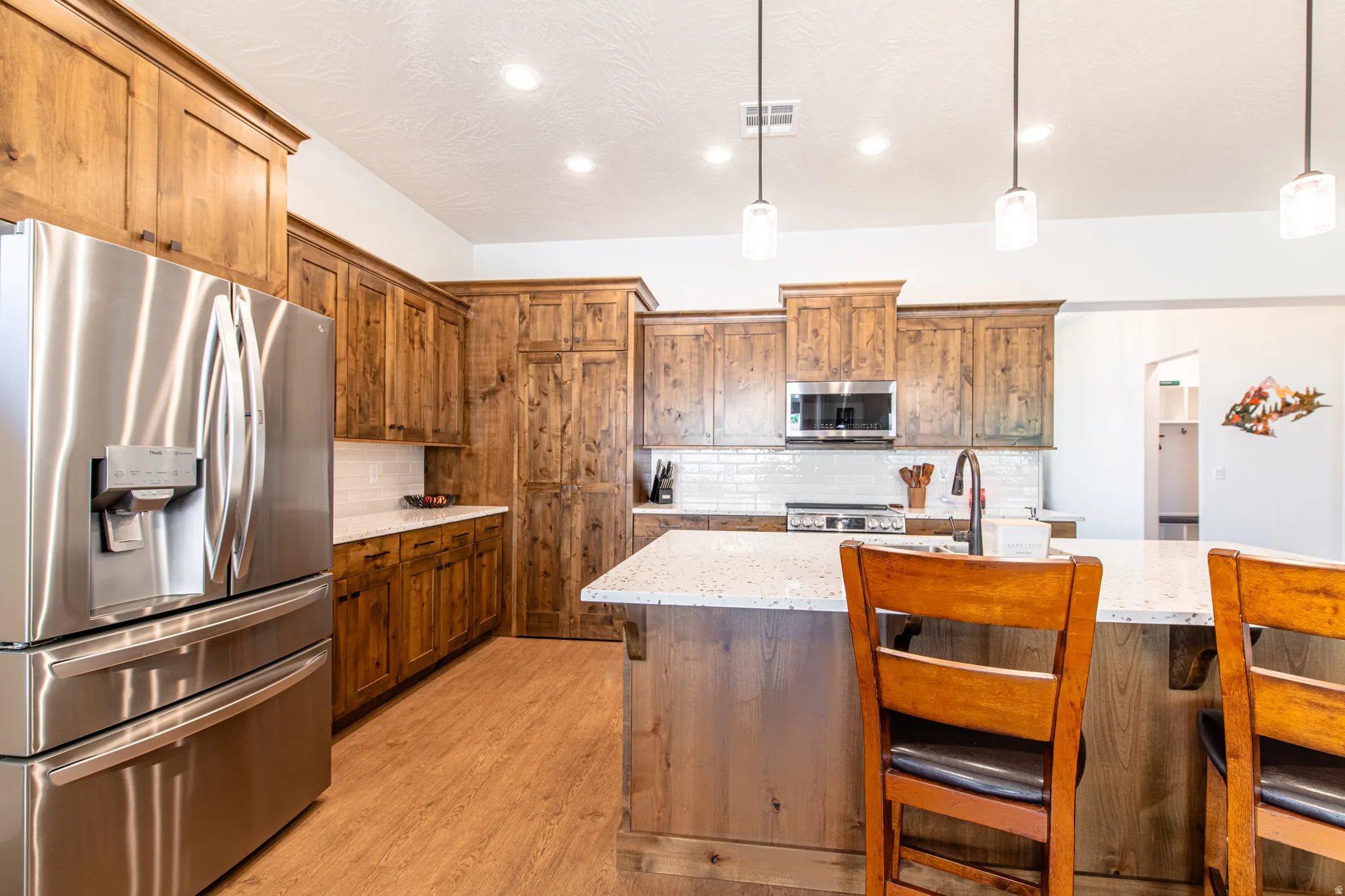 Kitchen featuring wood-finish cabinetry, stainless steel appliances, white subway tile backsplash, and a central island with a light-toned countertop