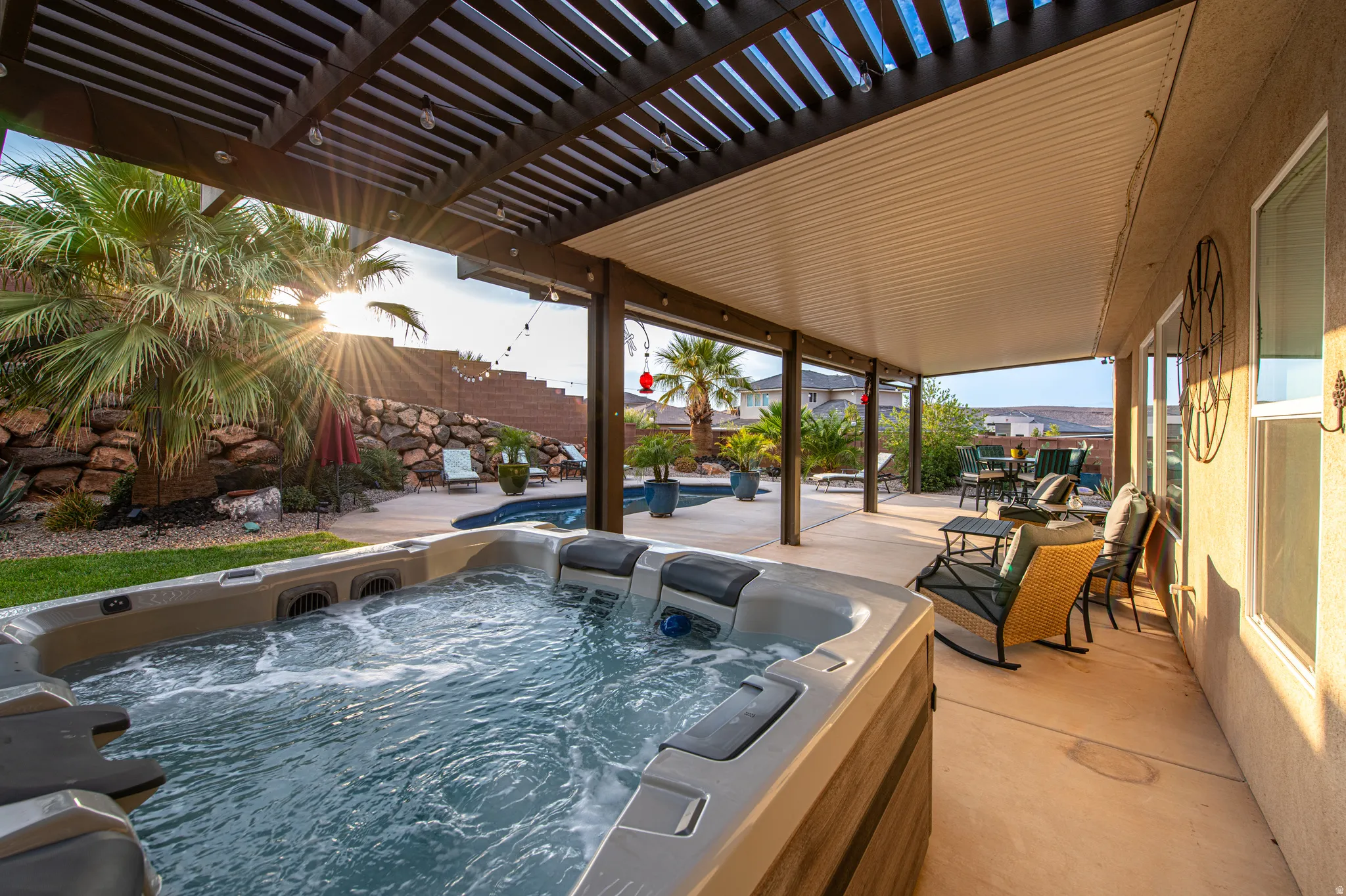 Spa with bubbling water, covered patio with slatted pergola, additional covered patio, concrete patio, and mature landscaping