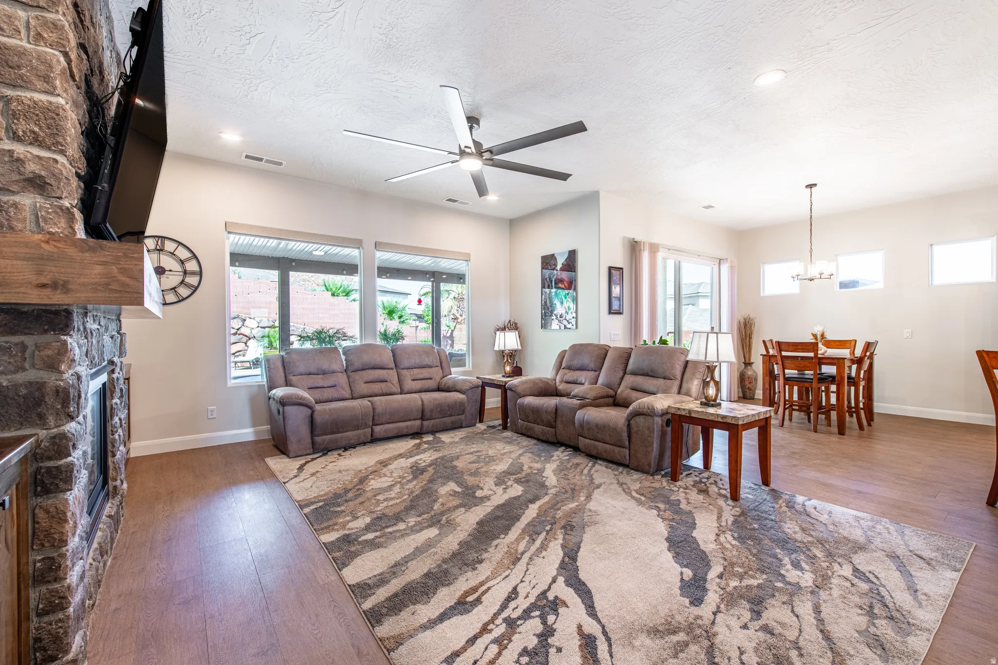 Stone-clad fireplace with a wood mantel, wood-finish flooring, recessed lighting, and a ceiling fan