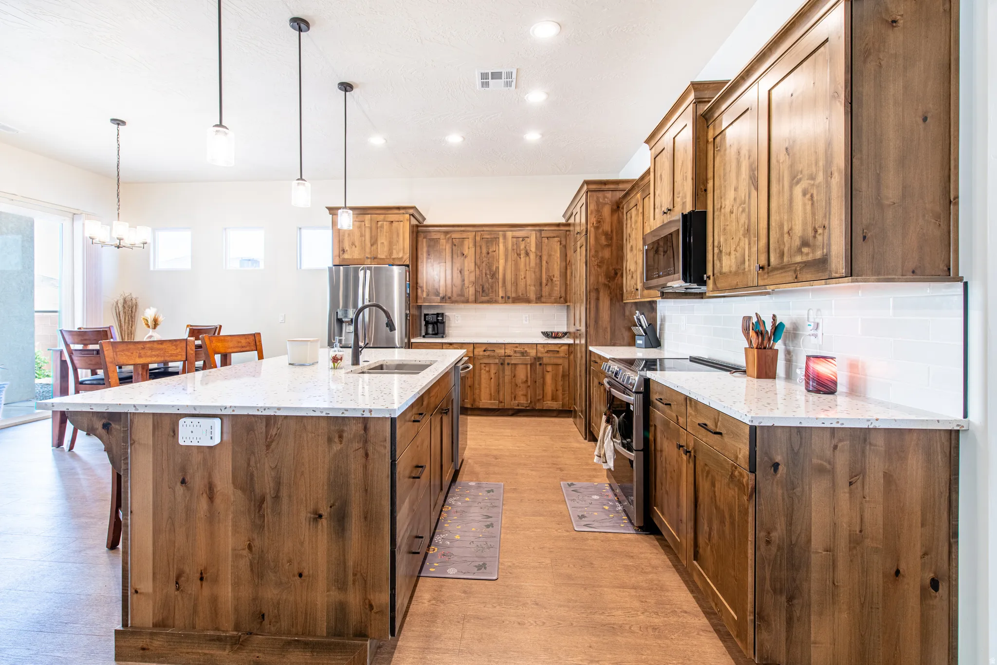 Kitchen featuring wood cabinetry, light-toned countertops, a stainless steel refrigerator, and pendant lighting