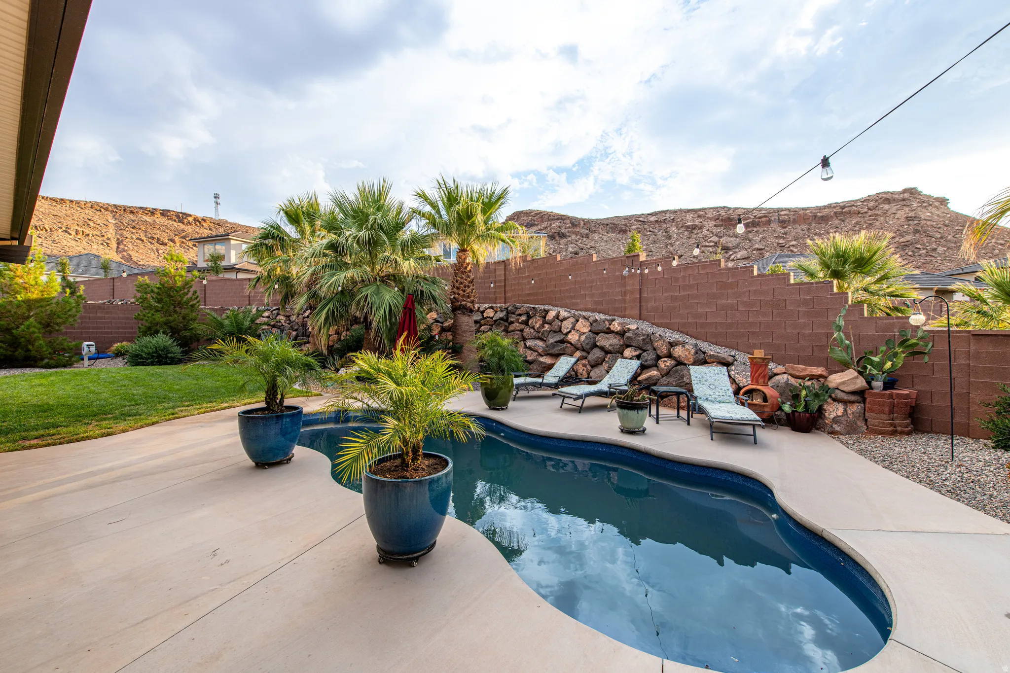 Freeform swimming pool with surrounding concrete patio, natural rock retaining wall, and mature palm trees
