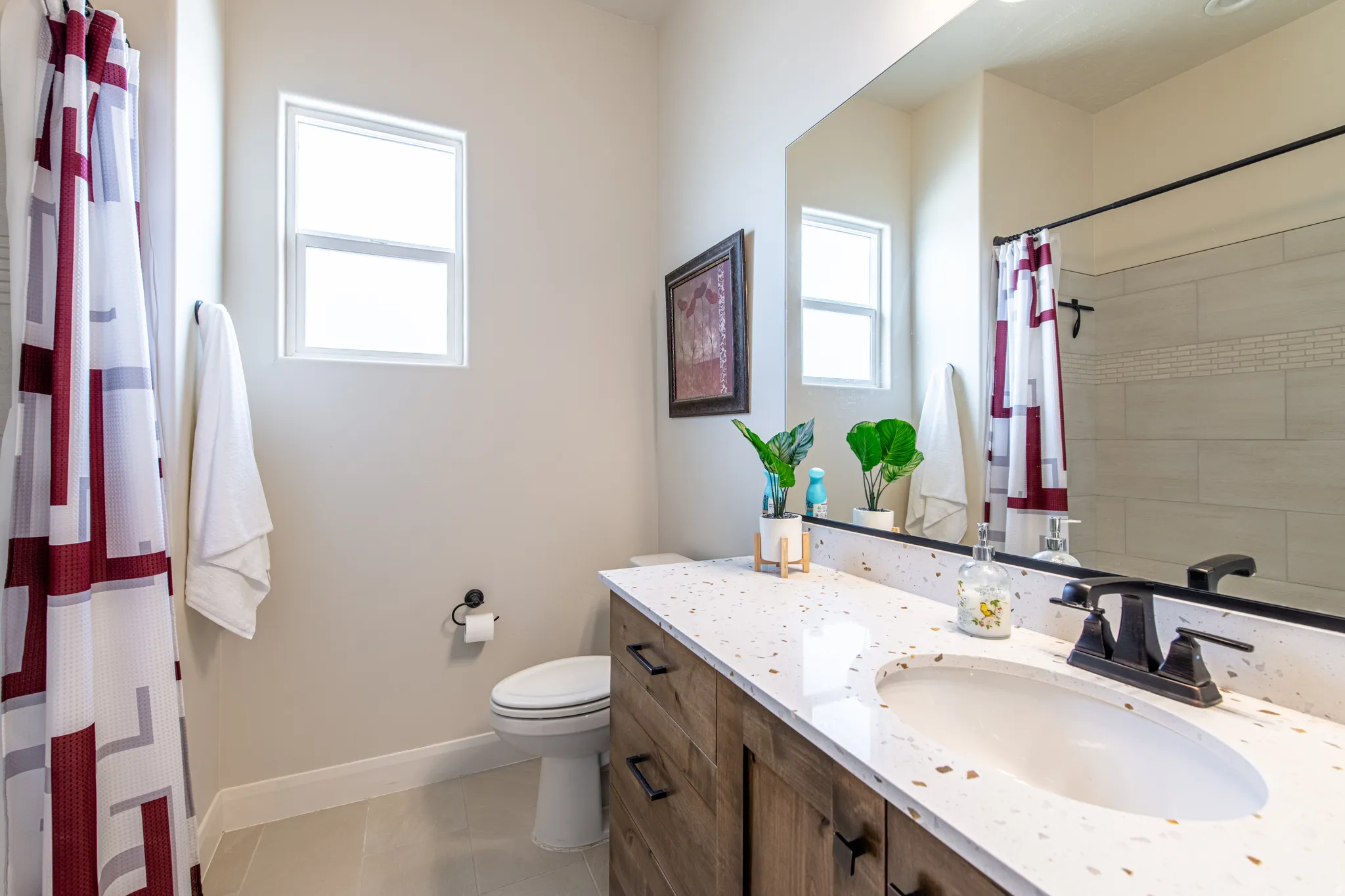 Bathroom featuring a single window, a wood-finish vanity with a built-in sink, a speckled countertop, and a shower with tiled walls