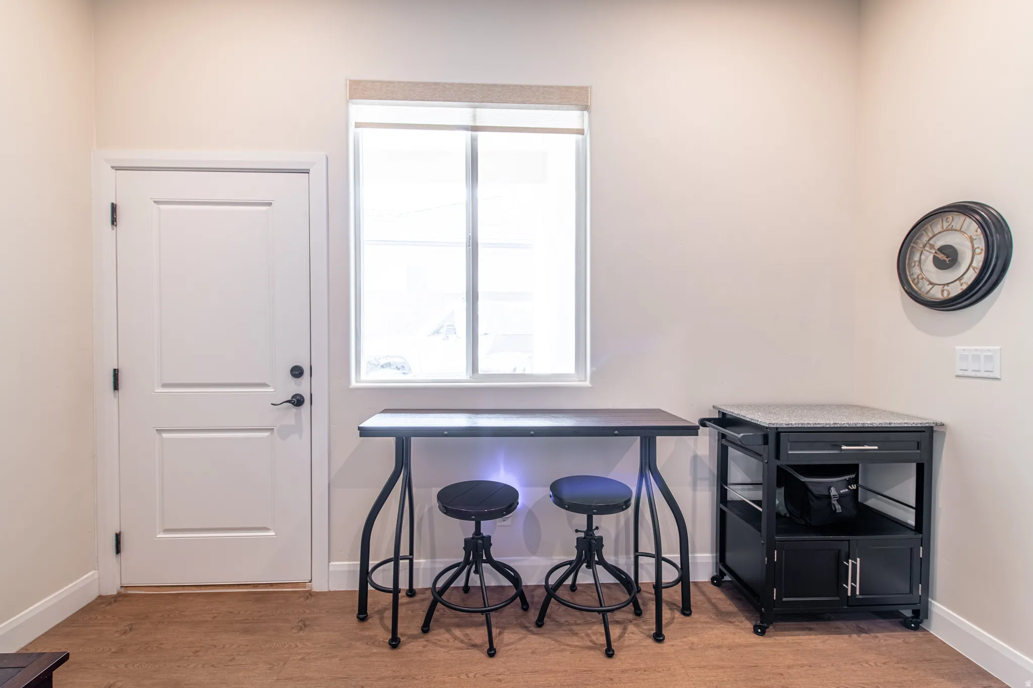 White paneled door with matte black hardware, single window with roller shade, wood-finish flooring, and light-toned wall paint