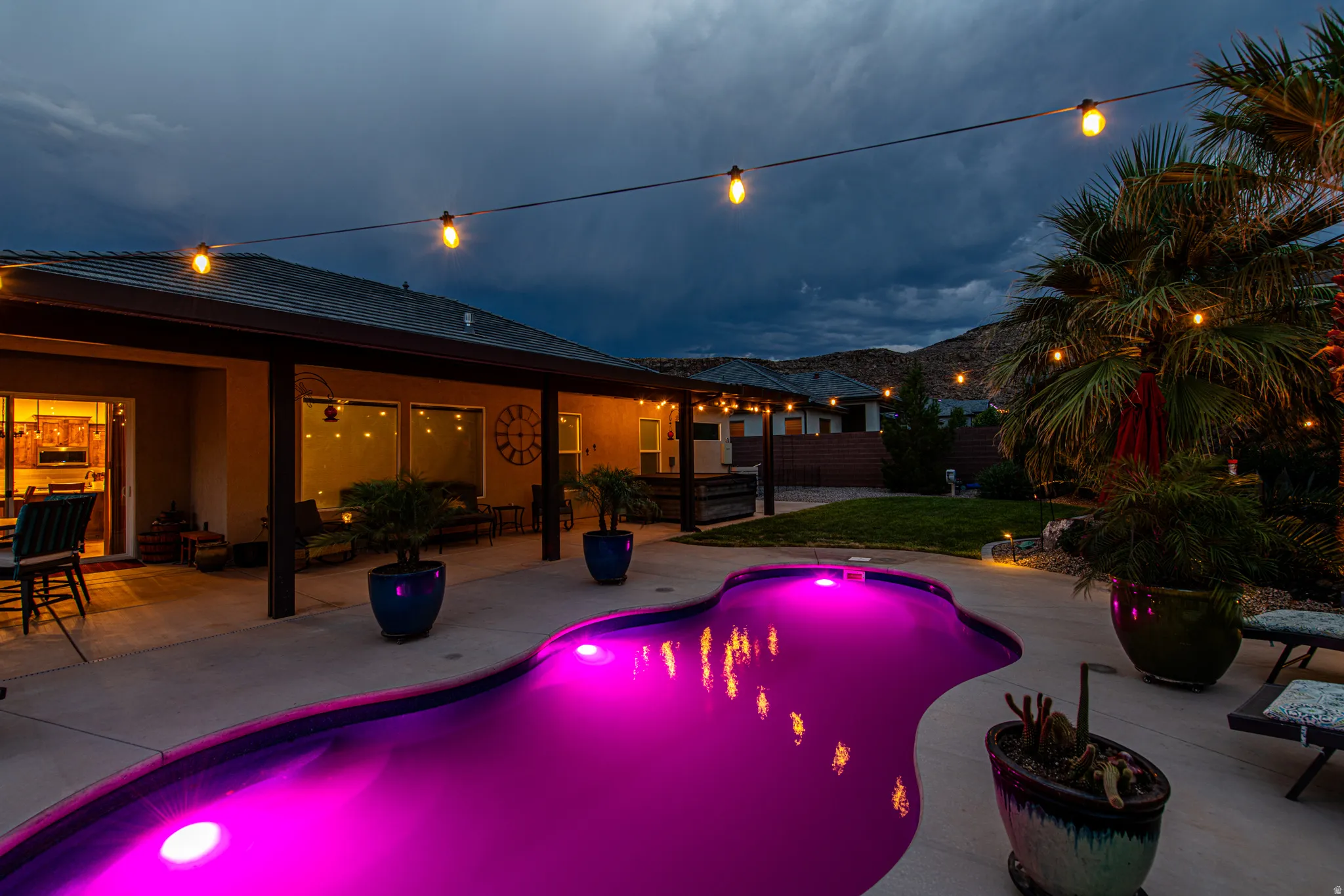 Resort-style backyard featuring a freeform pool with integrated lighting, a covered patio, string lights, and mature palm trees