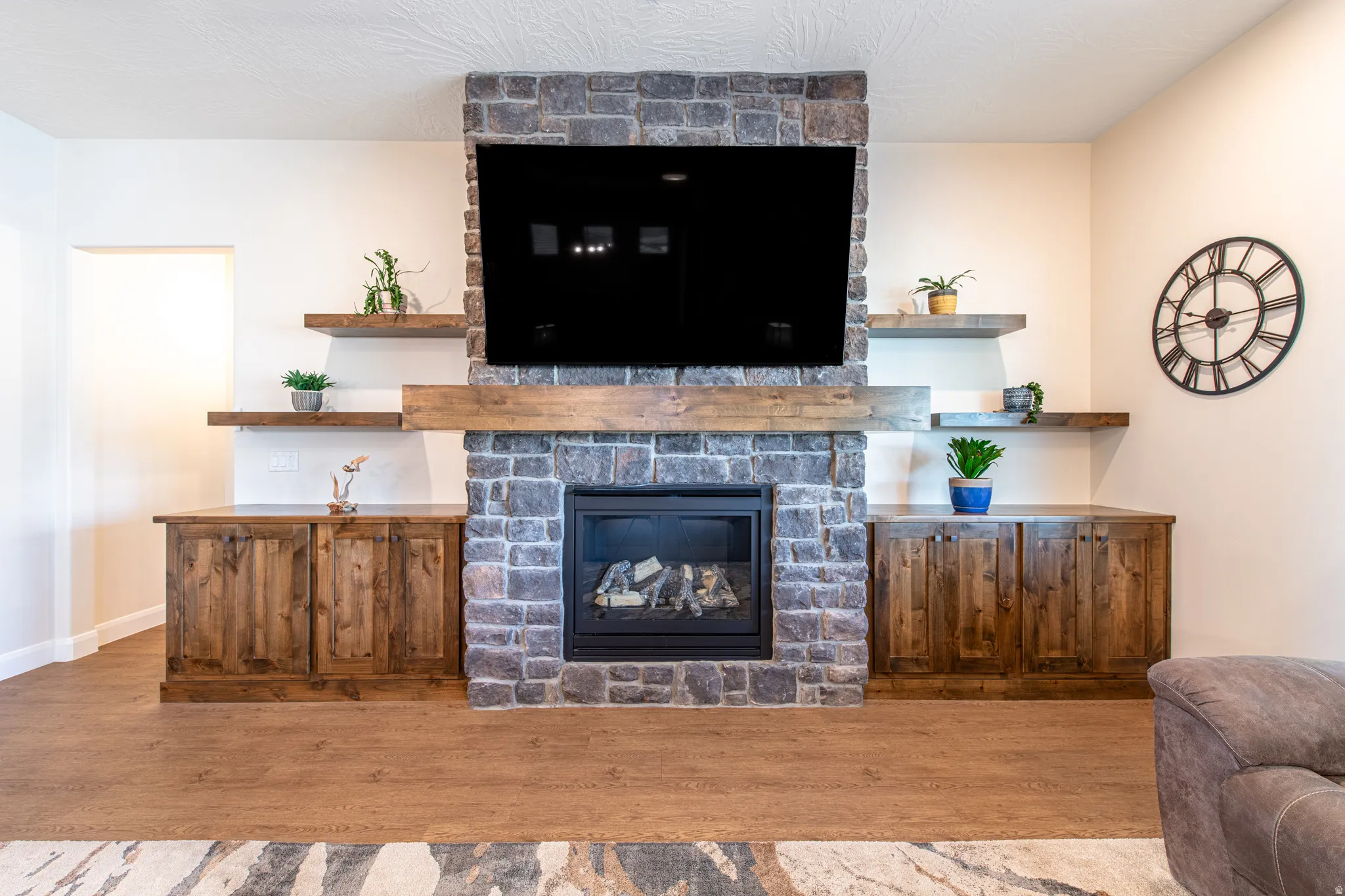 Stone-clad fireplace with a wood mantel, flanked by built-in wood cabinetry and floating shelves