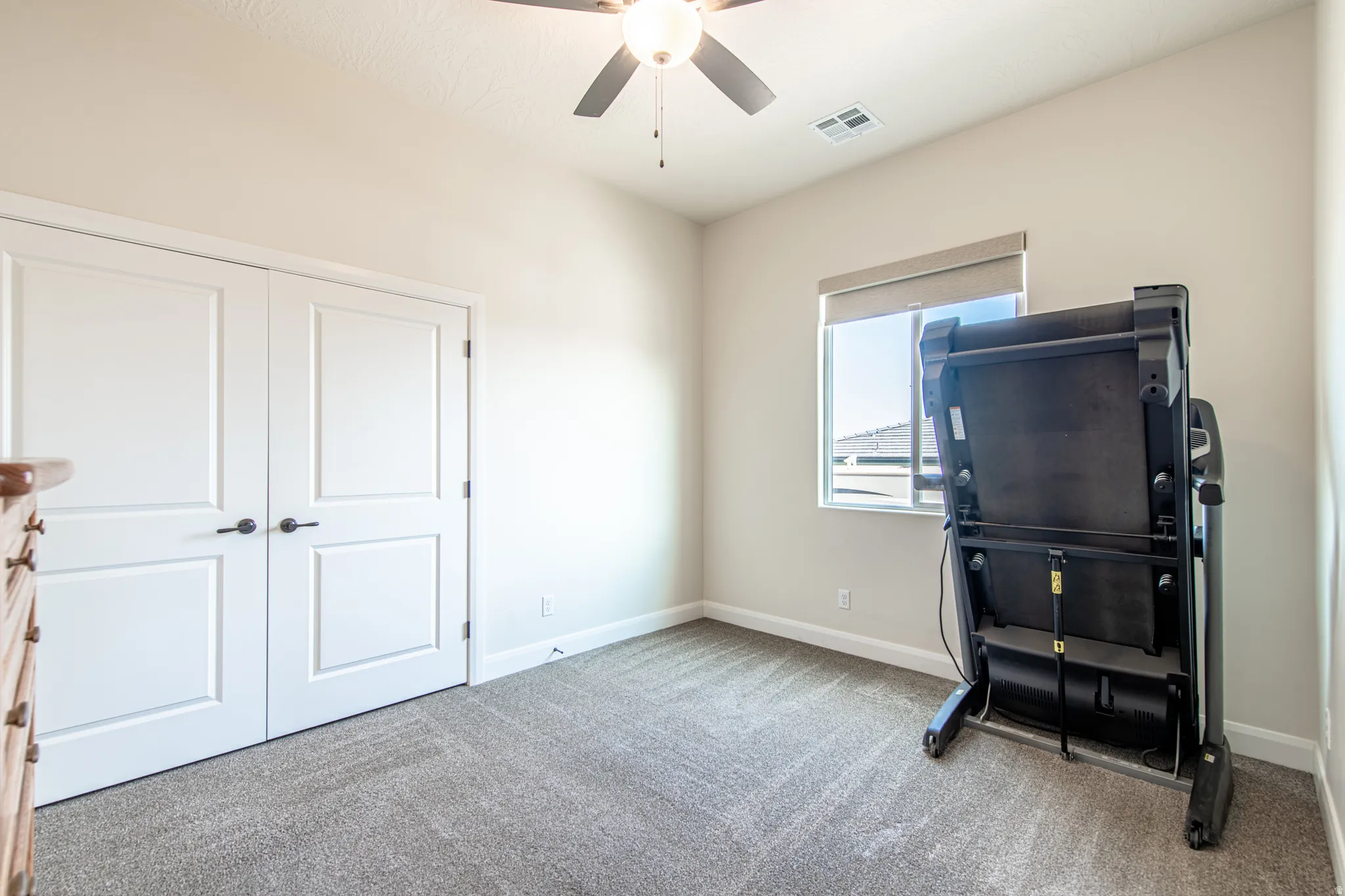 Recessed lighting, ceiling fan, neutral wall paint, carpet flooring, and a window with a roller shade