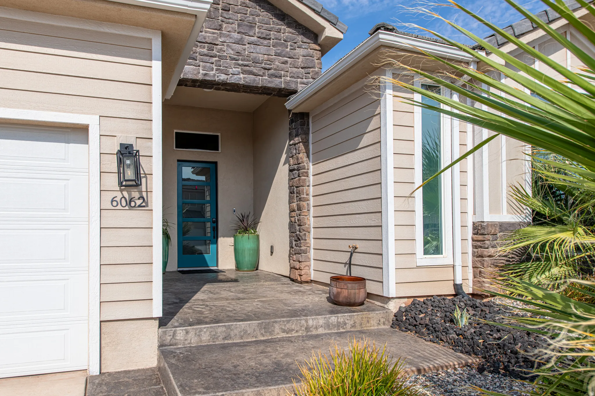 Stone accent façade with horizontal siding, a paneled garage door, and a vibrant teal front entry door