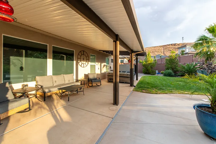 Expansive covered patio with concrete flooring, multiple large windows, and a landscaped backyard featuring a manicured lawn