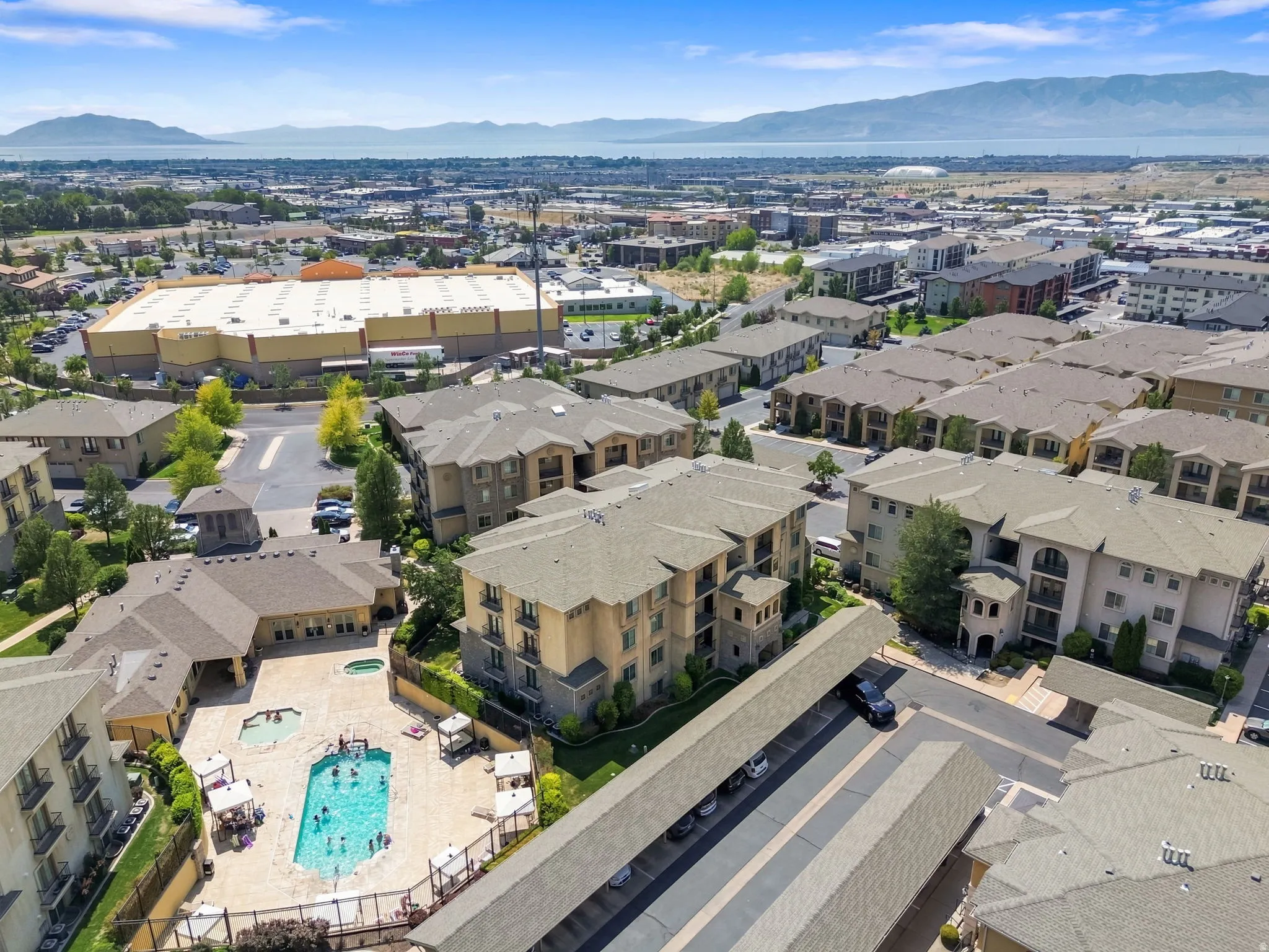 Outdoor swimming pool with integrated spa and surrounding paved sundeck, covered parking structures, and multi-story residential buildings with balconies