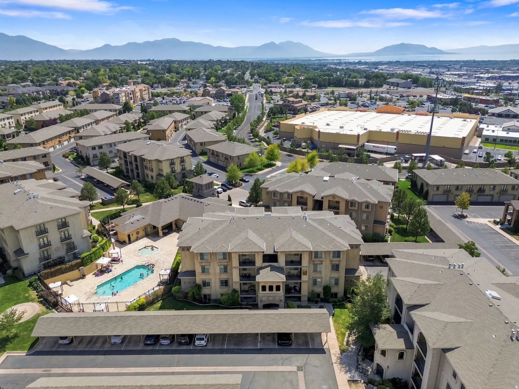 Aerial view showcasing a multi-unit residential complex with resort-style amenities including a sparkling swimming pool, mature landscaping, and ample surface parking