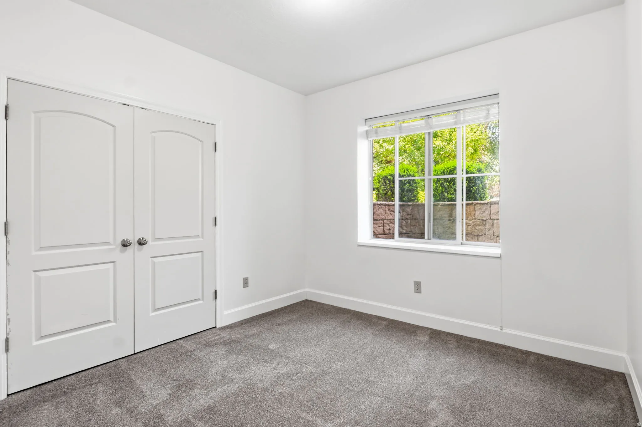 Neutral gray carpeting, white walls, and a window with blinds