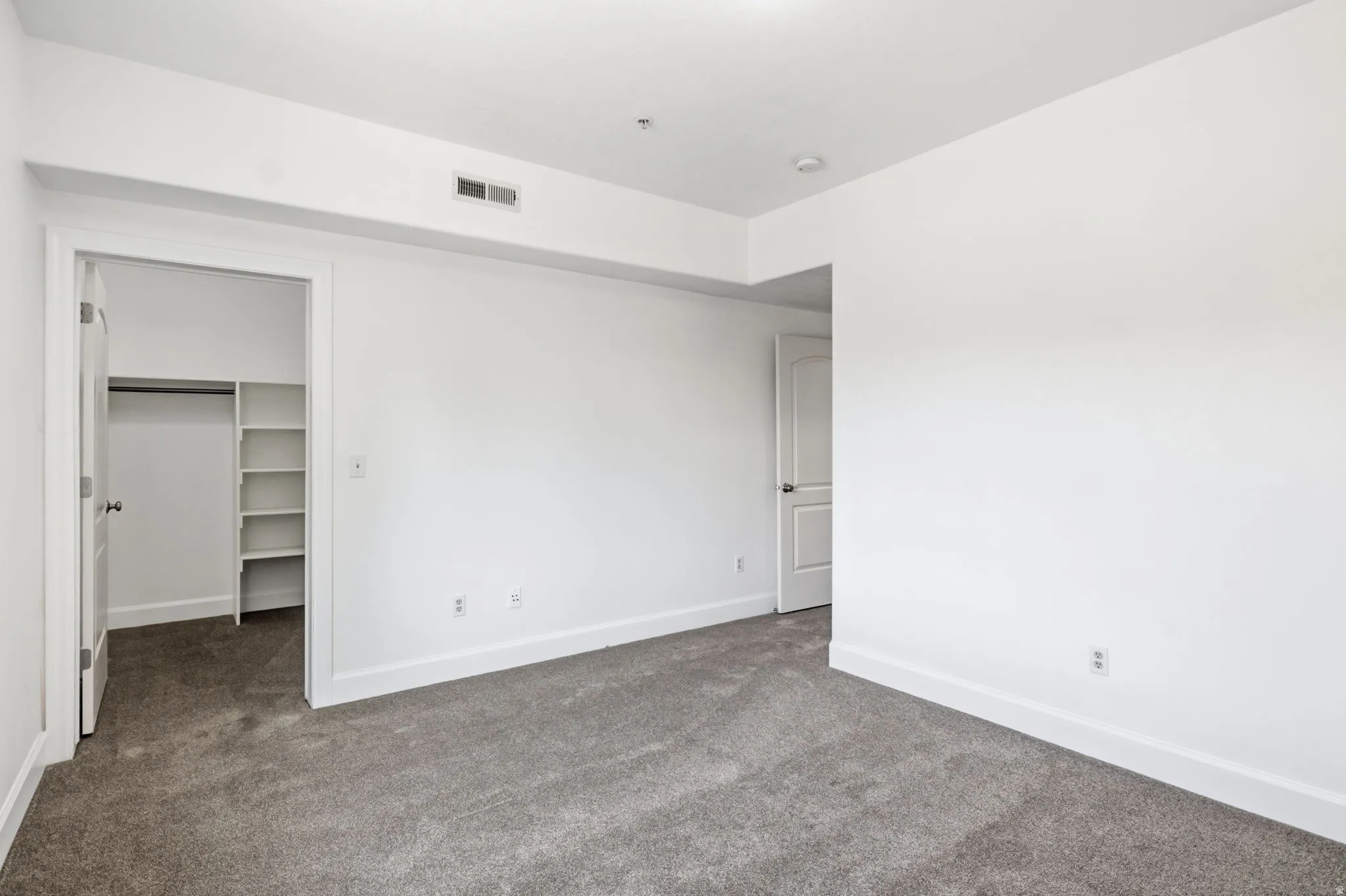 Neutral white wall finish, recessed overhead lighting, gray carpet flooring, white interior doors, and built-in closet shelving
