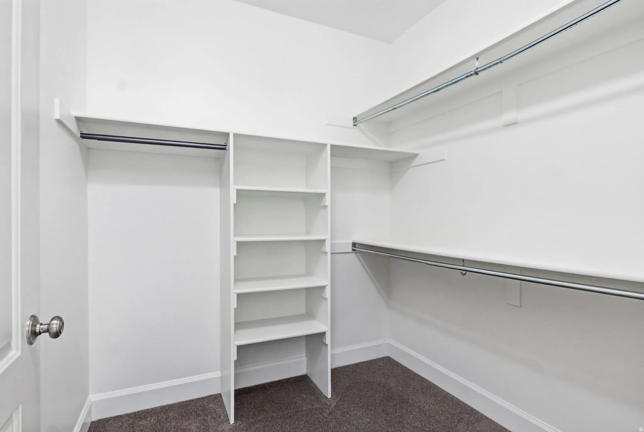 Walk-in closet with built-in shelving, multiple hanging rods, and dark carpet flooring