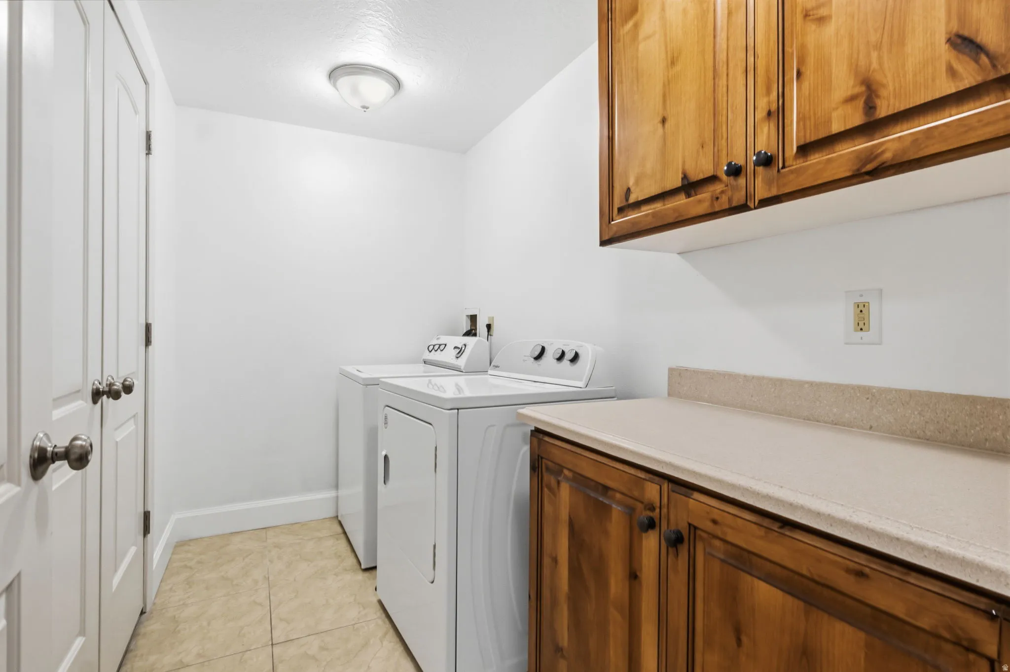 Laundry area featuring wood cabinetry, light-toned countertop, and durable tile flooring