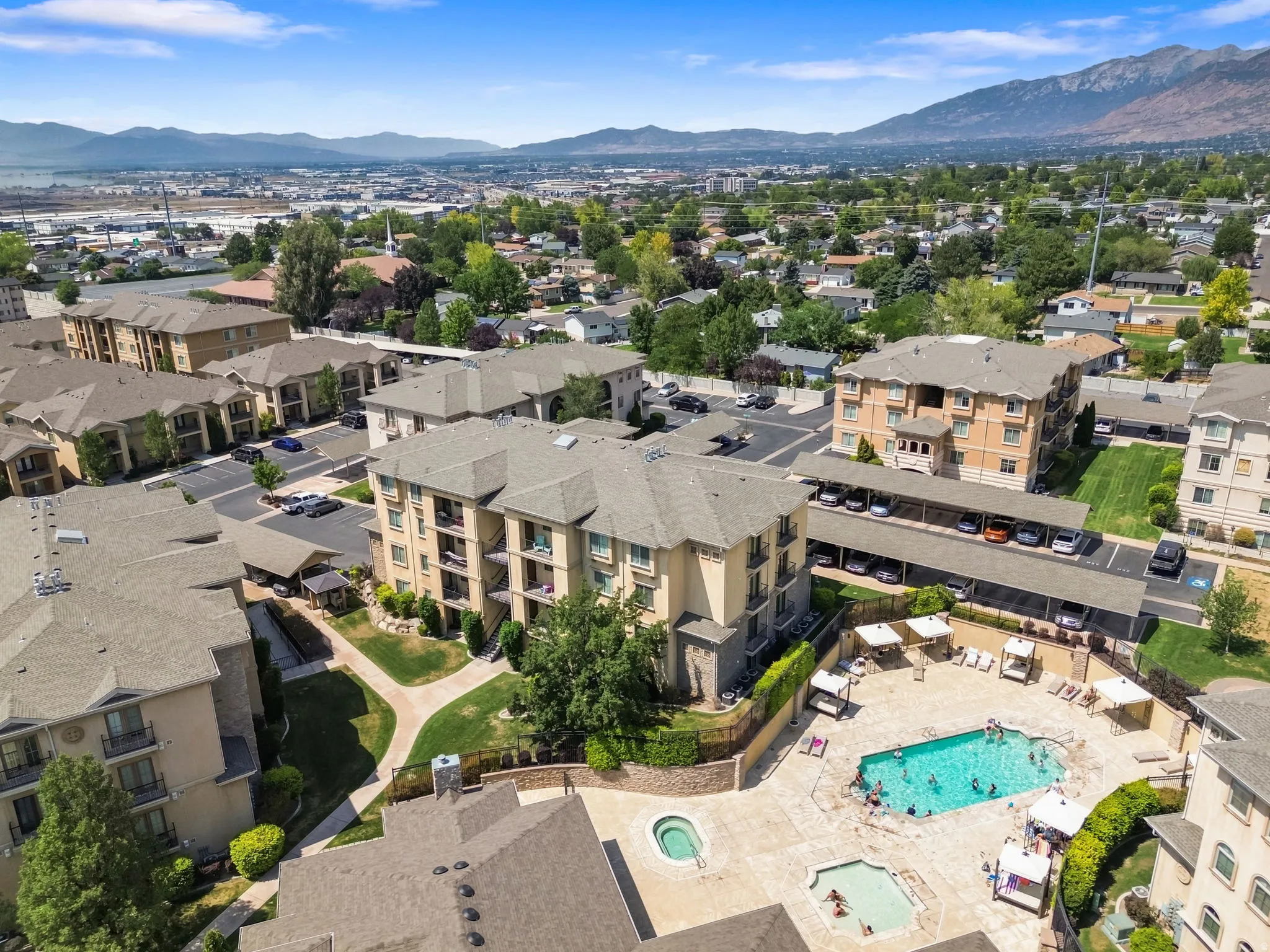 Community featuring multiple residential buildings, a central swimming pool with surrounding patio, and dedicated covered parking
