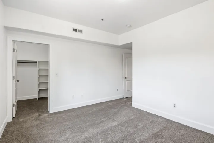 Neutral white wall finish, recessed overhead lighting, gray carpet flooring, white interior doors, and built-in closet shelving