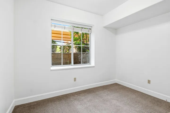 Bright interior with white walls, window with blinds, and brown carpet flooring