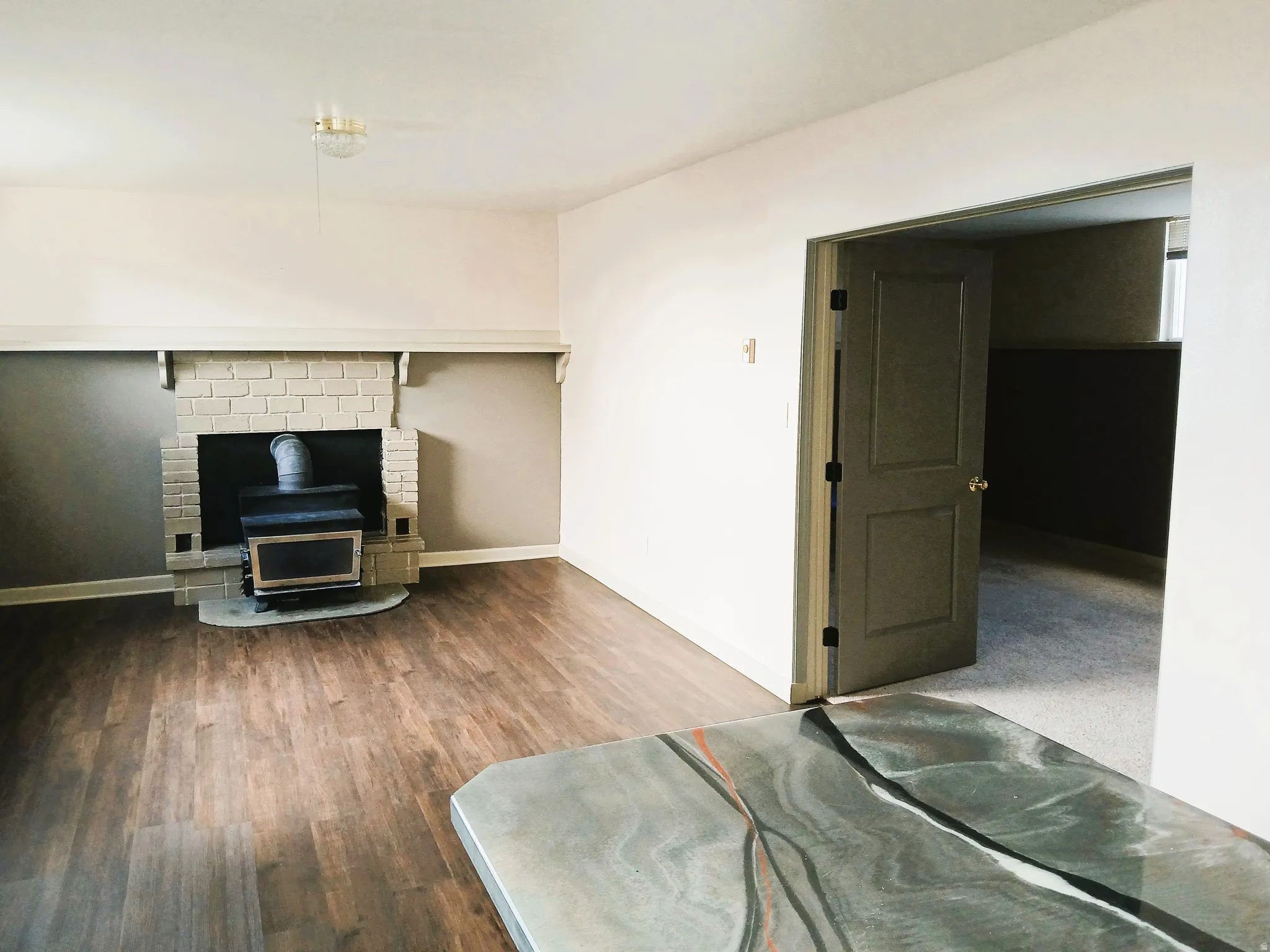 Wood-finish flooring, brick fireplace with wood-burning stove, and a doorway leading to a carpeted room