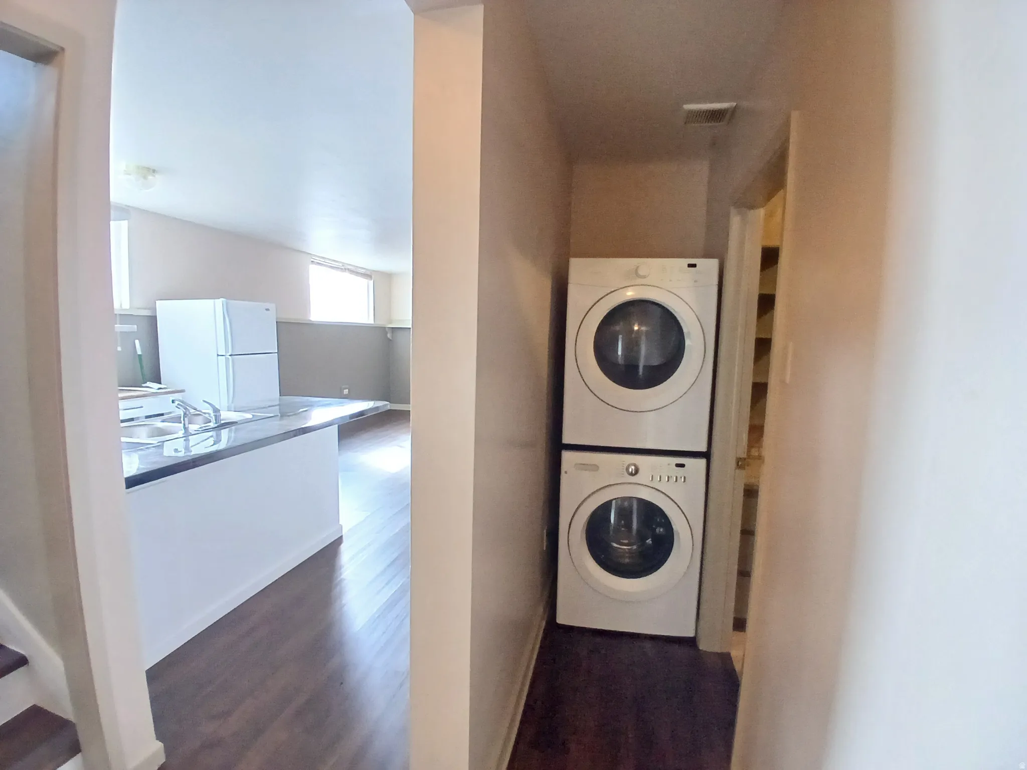 Stacked washer and dryer unit, wood-finish flooring, and a kitchen island with an integrated sink