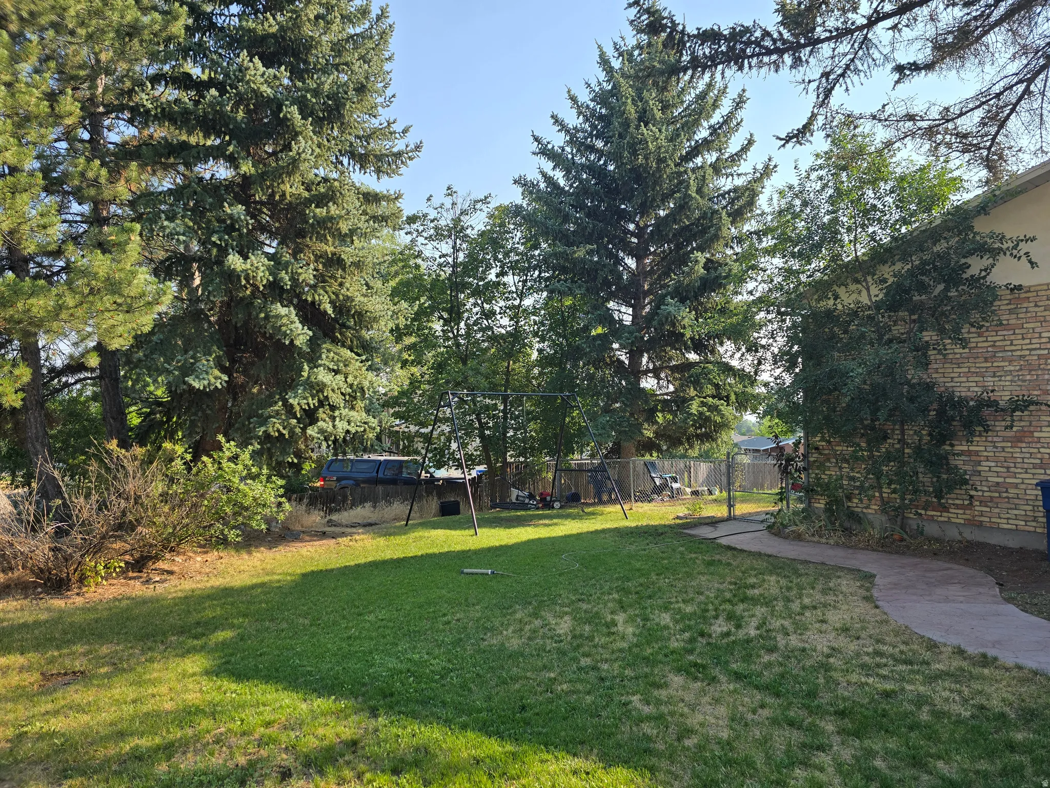 Expansive lawn area with mature trees and a concrete pathway leading to a fenced perimeter