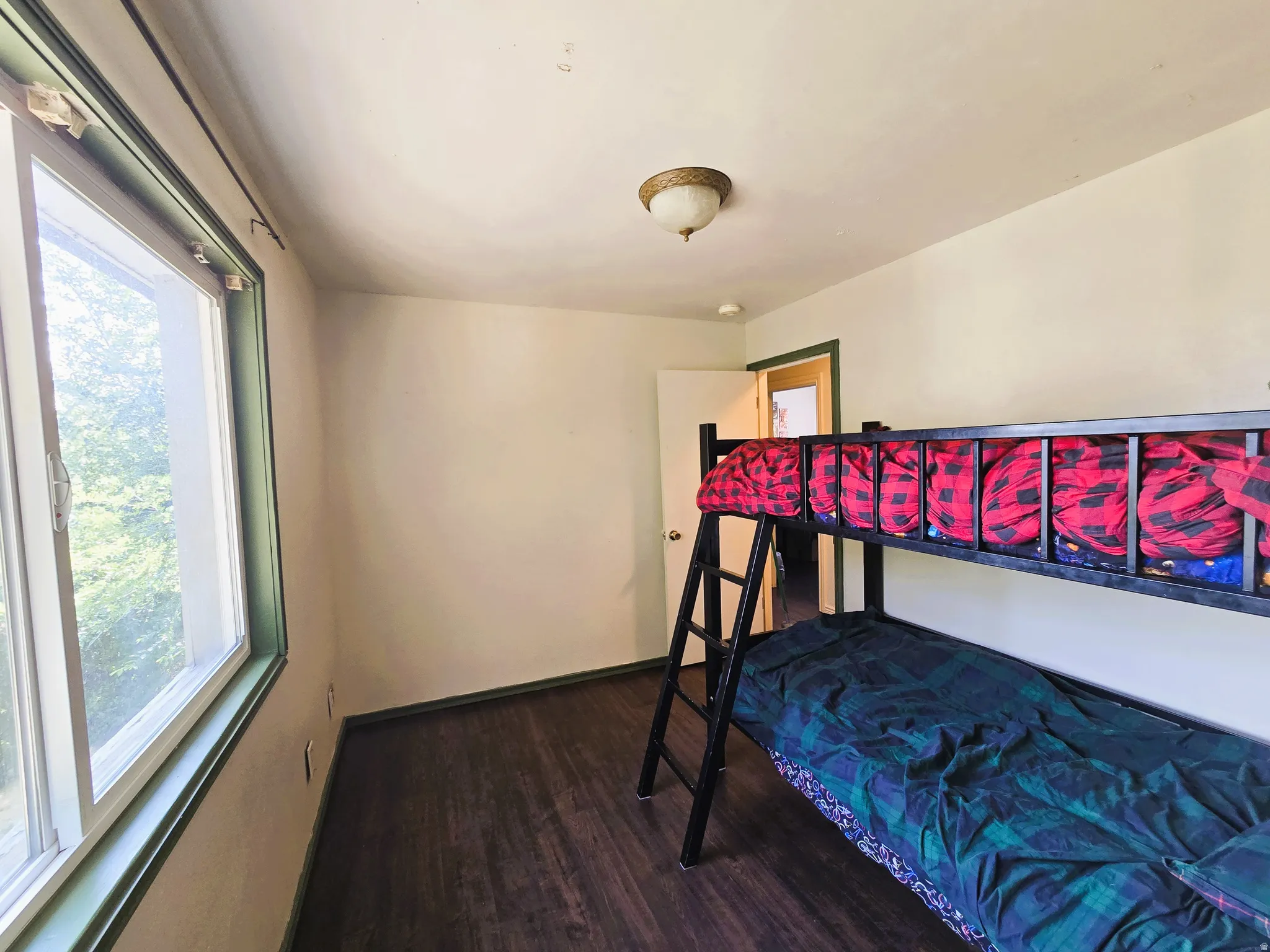 Room featuring wood-finish flooring, a window with green trim, and a ceiling-mounted light fixture