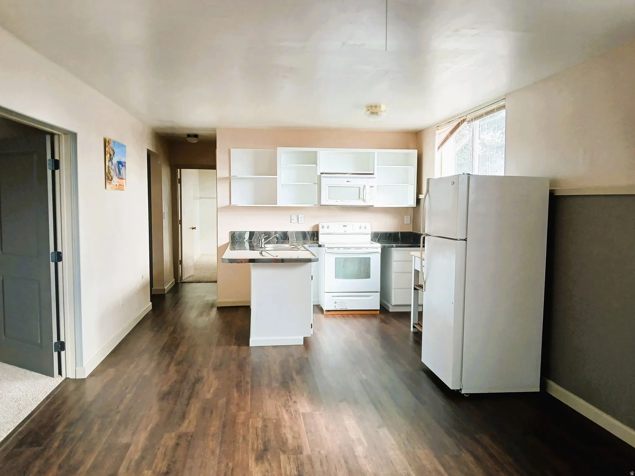 Kitchen with white appliances, white cabinetry, dark wood-finish flooring, and a stainless steel sink