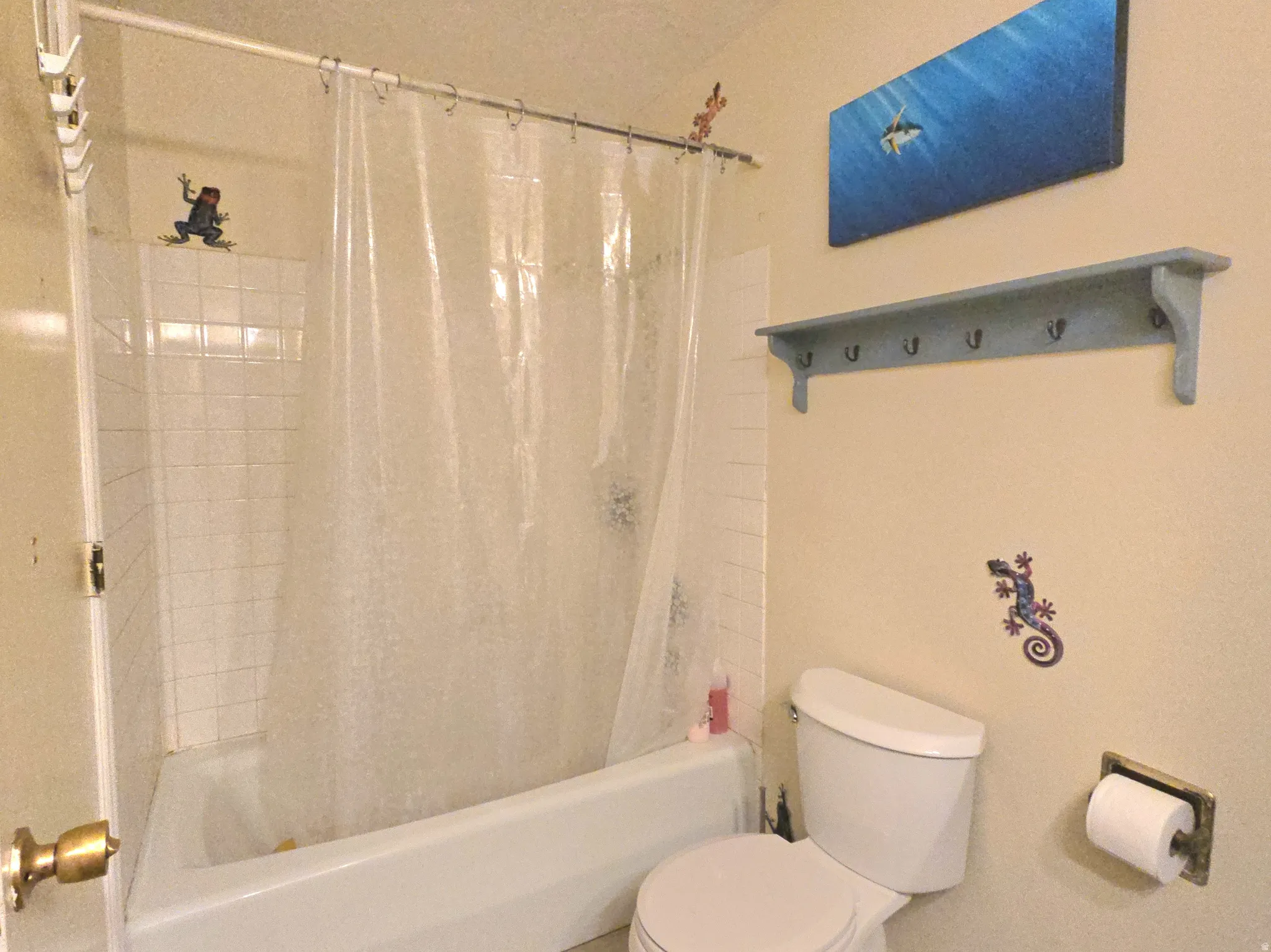 Bathtub with white tile surround, white toilet, and wall-mounted shelving with hooks