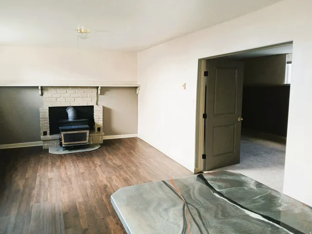 Wood-finish flooring, brick fireplace with wood-burning stove, and a doorway leading to a carpeted room