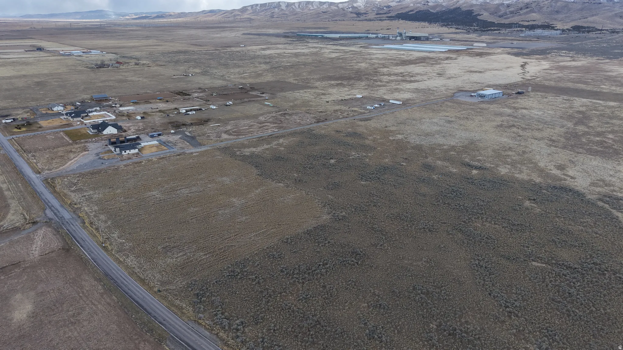 Expansive rural setting with a paved road, scattered residential structures, and distant mountainous terrain