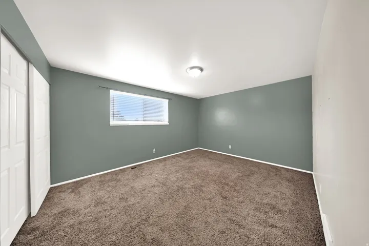 Plush carpet flooring, neutral paint palette, window with horizontal blinds, flush mount ceiling light, and bi-fold closet doors