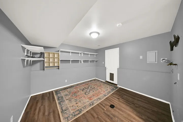 Wood-finish flooring, white permanent shelving, built-in cubby storage, white paneled door, and overhead lighting