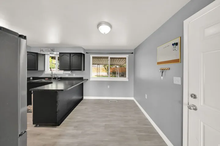 Kitchen featuring wood-finish flooring, dark cabinetry, dark countertops, and a stainless steel refrigerator