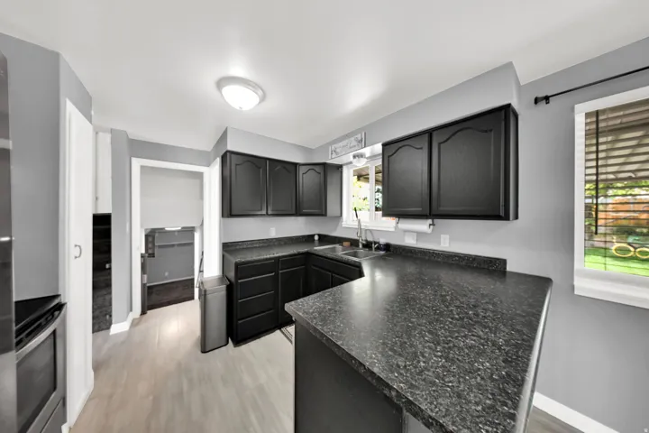 Kitchen featuring dark cabinetry, dark speckled countertops, wood-finish flooring, and a window above the sink