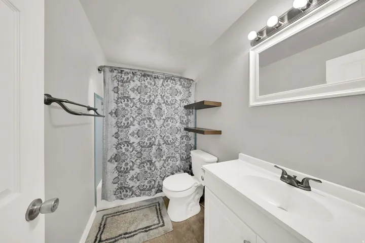 Vanity with integrated sink, wall-mounted mirror, overhead lighting fixture, and floating shelves