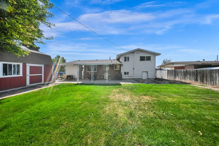 Expansive grassy yard area with a red barn-style shed, covered patio, rear siding, and wood fencing