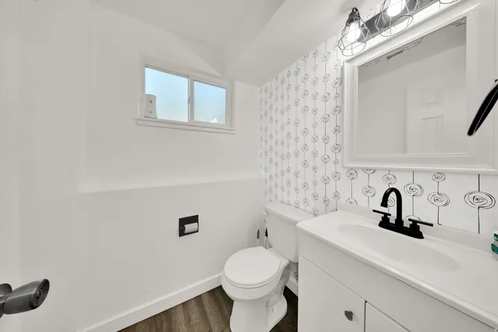 Bathroom featuring a white vanity with integrated sink, black fixtures, an illuminated mirror, and wood-finish flooring