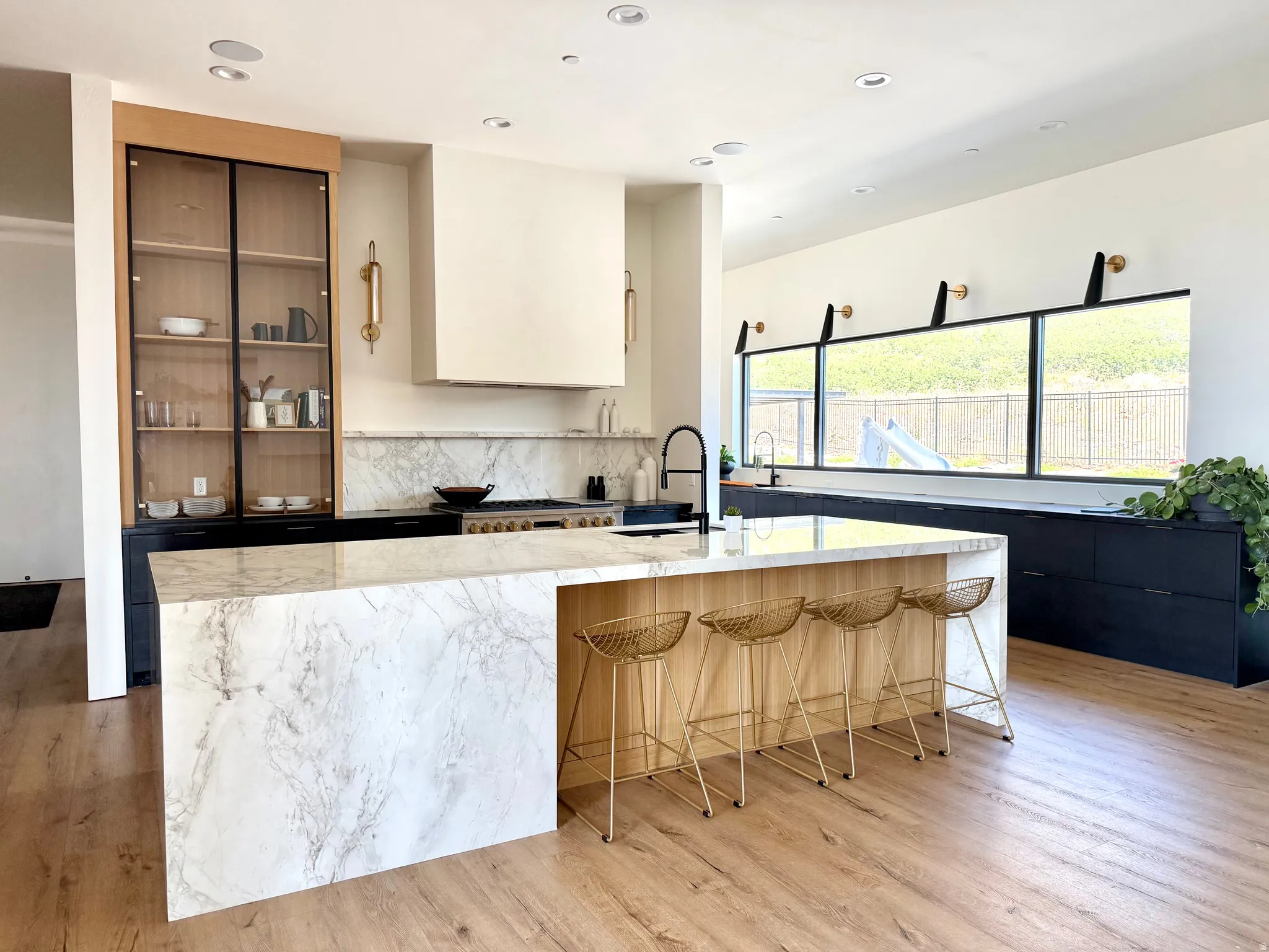 Expansive kitchen featuring a waterfall island, wood-finish flooring, custom cabinetry, a built-in range hood, and a series of horizontal windows