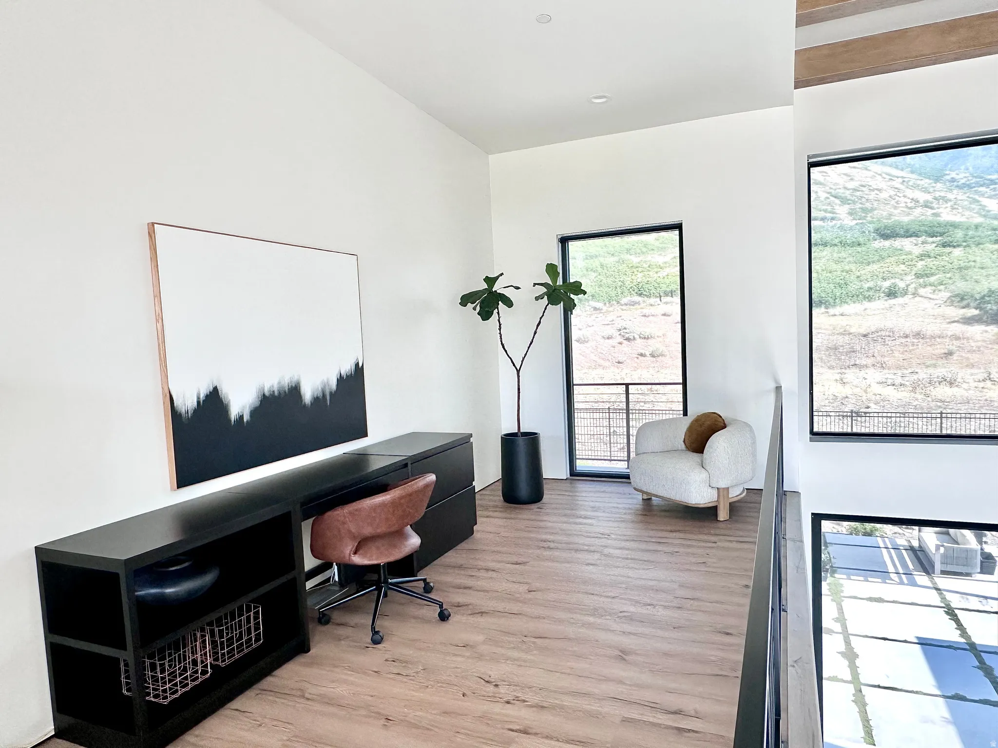Wood-finish flooring, high ceilings, large windows with black frames, and a black metal railing