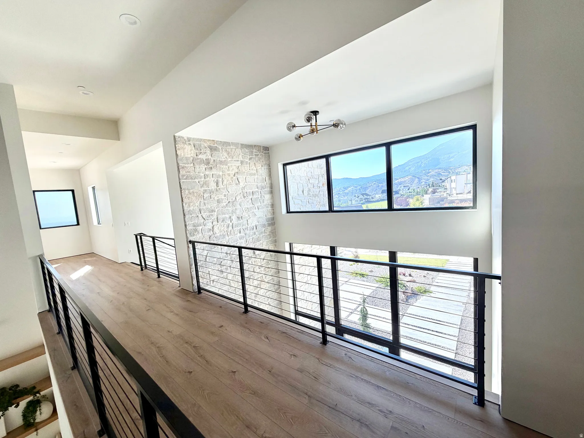 Wood-finish flooring throughout, modern cable railing system, stone accent wall, recessed lighting, and large windows with black frames
