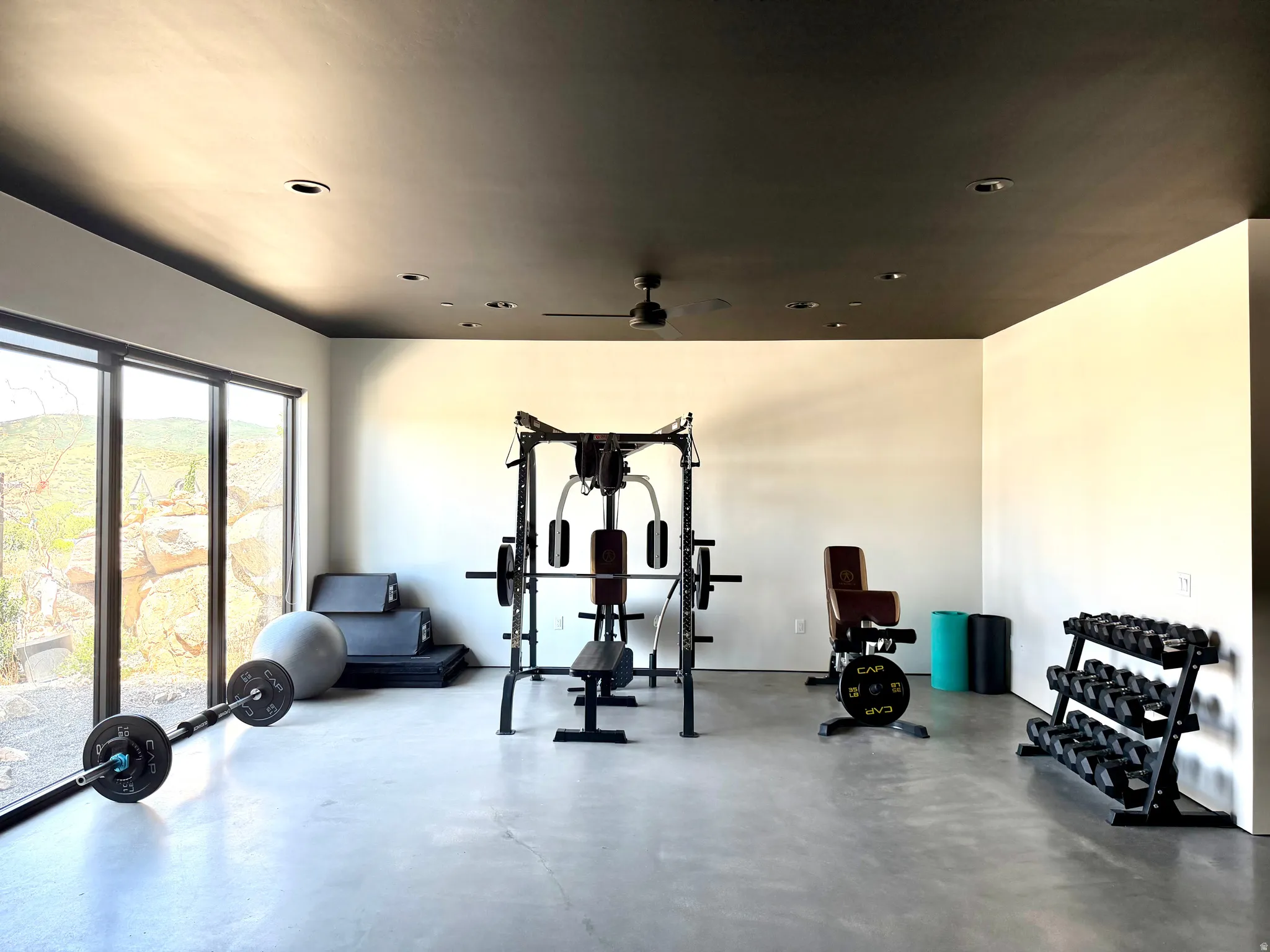 Polished concrete flooring, recessed lighting, ceiling fan, and large-format windows with roller shades